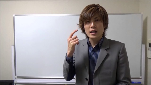 灰色スーツで手を挙げ説明する本人(動画「台打ち、打ち子のお願いの仕方」より)
