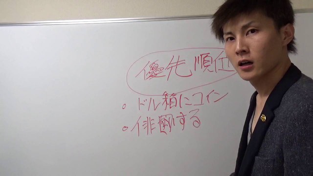 ホワイトボードの「優先順位」を指す本人(動画「優先順位を考えてスピードアップ!【パチスロ】…」より)